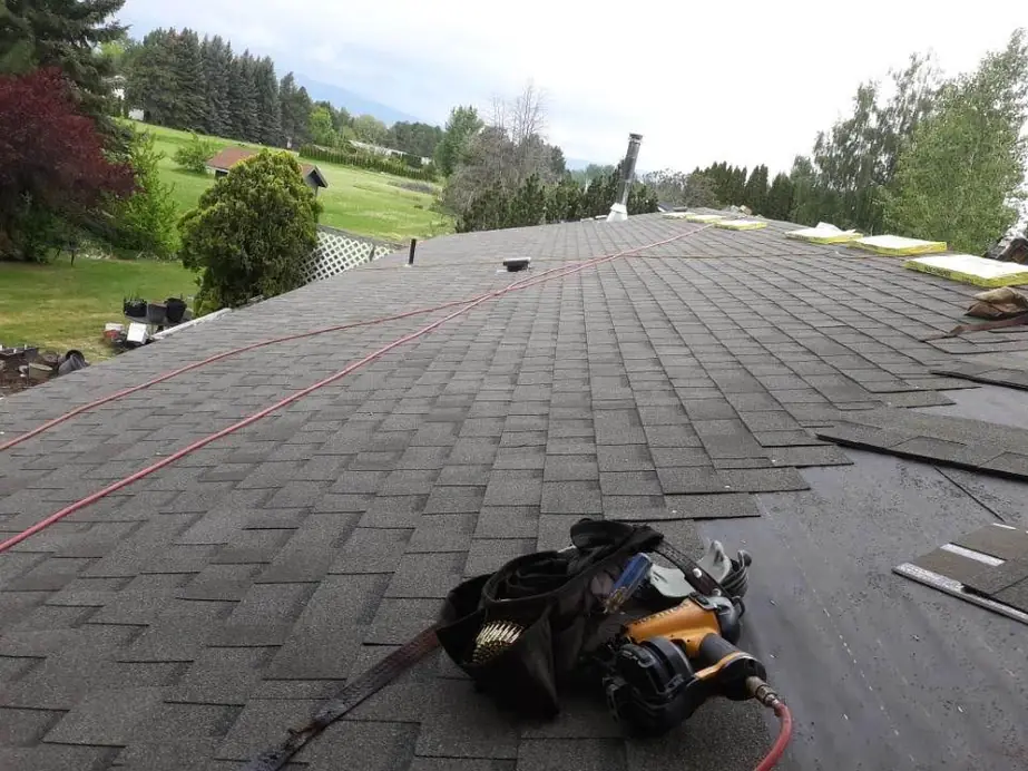 Superior Roofing job in progress: new charcoal shingles going down, red air hoses and a coil nailer on the deck, green hills behind