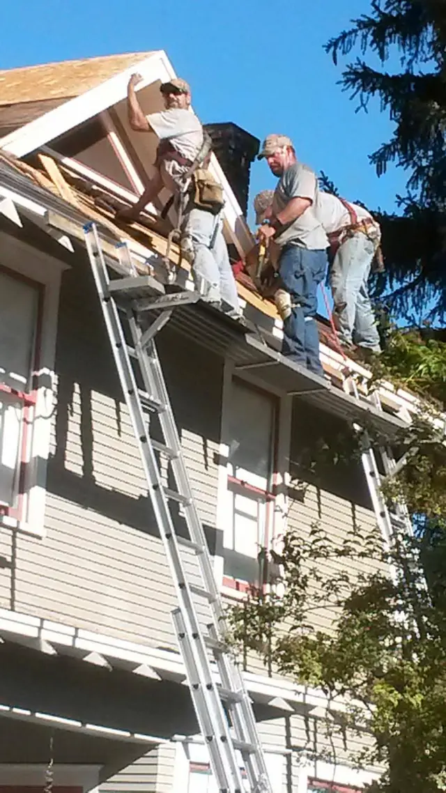 Superior Roofing crew in harnesses tearing off a gable roof on a two-storey house